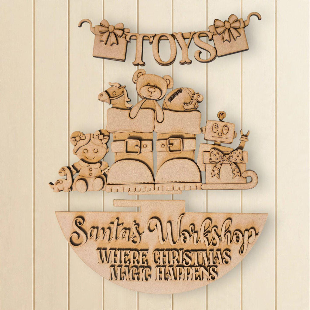 A wooden sign with the text "Toys" and "Santa's Workshop Where Christmas Magic Happens" carved into it, along with various toys and decorations.