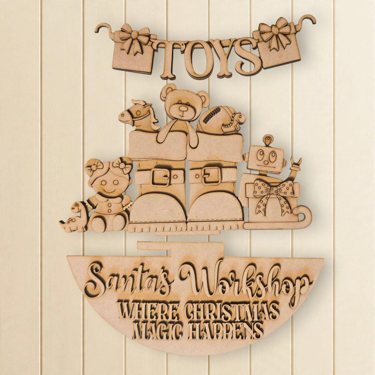 A wooden sign with the text "Toys" and "Santa's Workshop Where Christmas Magic Happens" carved into it, along with various toys and decorations.