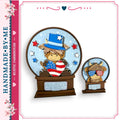 two snow globes, each containing a cartoon character wearing patriotic attire. The character in the larger snow globe is wearing a hat and holding an American flag, while the character in the smaller snow globe is wearing sunglasses and holding a moo. The snow globes are set against a blue background with stars and red and white stripes.