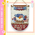 a wooden sign with patriotic decorations, including an eagle wearing sunglasses and holding an American flag. The sign is hanging on a wall and has a message that reads "Land of the free, because of the brave".