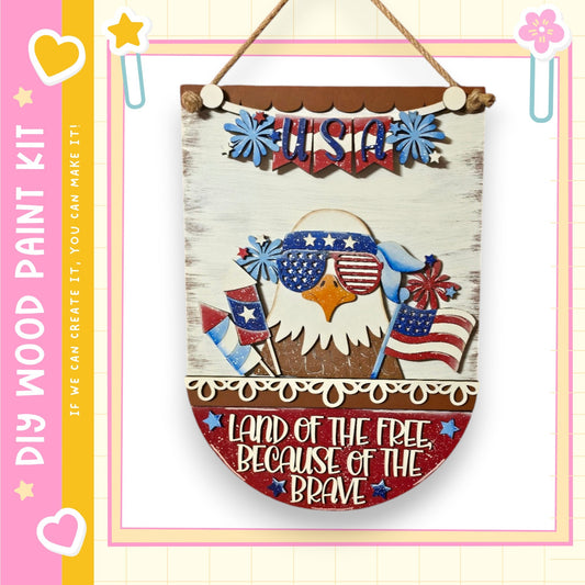 a wooden sign with patriotic decorations, including an eagle wearing sunglasses and holding an American flag. The sign is hanging on a wall and has a message that reads "Land of the free, because of the brave".