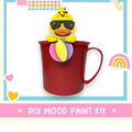 A red mug with a yellow duck wearing sunglasses, surrounded by various colorful stickers and hearts, with the text "DIY WOOD PAINT KIT" displayed.