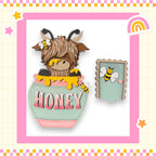 A cartoon image of a horned, furry animal with a honey pot on its back, surrounded by a pink and yellow border with stars and a rainbow.