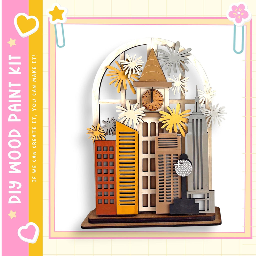 A wooden paint kit featuring a miniature city scene with various buildings, a clock, and decorative elements such as flowers and stars.
