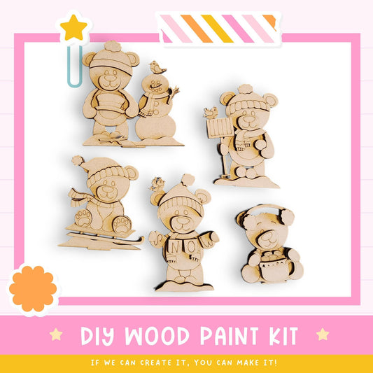 The image is a DIY wood paint kit featuring various wooden animal figures, including bears and a snowman, set against a pink and white background.