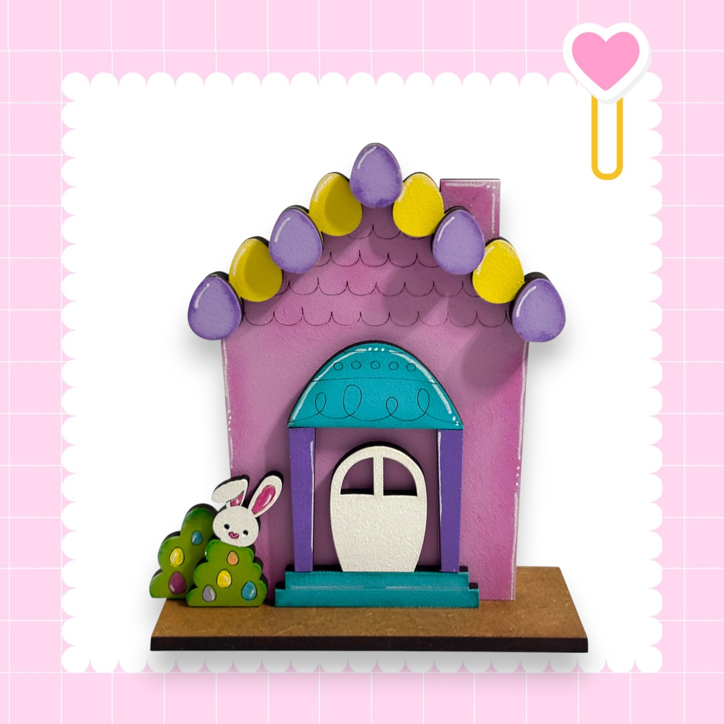 A colorful Easter-themed house with a bunny decoration, set against a pink background with a heart symbol.