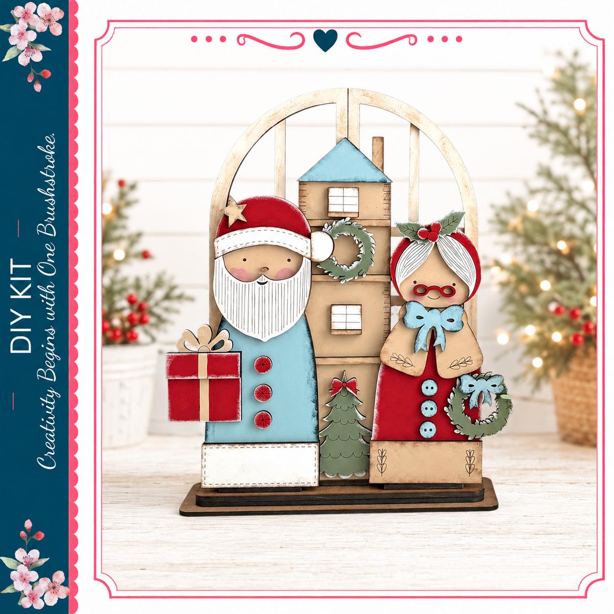A wooden Christmas tree ornament featuring Santa Claus and an elderly woman, with a wreath and gift box. The ornament is displayed on a wooden base, and the background includes a blurred Christmas tree and other holiday decorations.