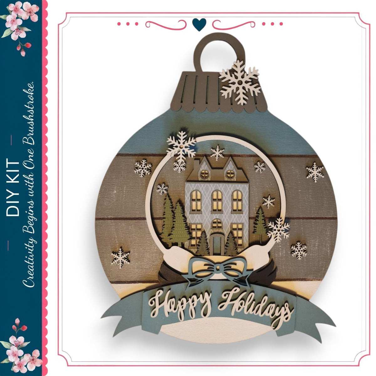 A decorative ornament with a snow globe containing a house and trees, surrounded by snowflakes. The ornament has a ribbon with the text "Happy Holidays" and a heart symbol.