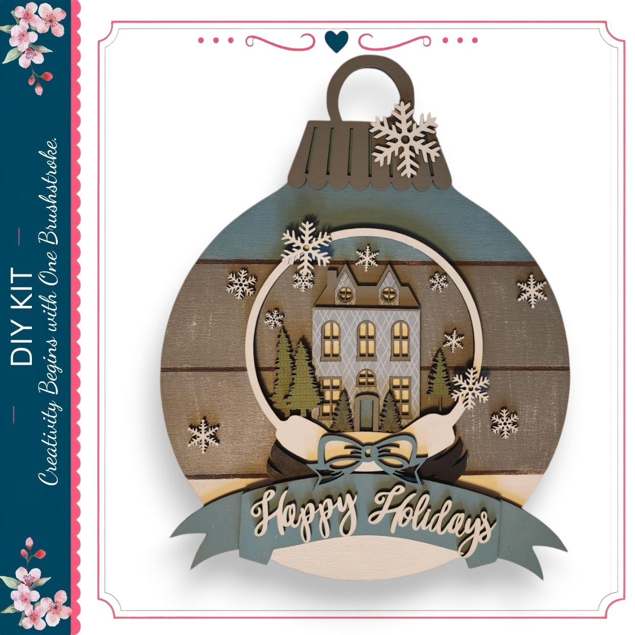 A decorative ornament with a snow globe containing a house and trees, surrounded by snowflakes. The ornament has a ribbon with the text "Happy Holidays" and a heart symbol.