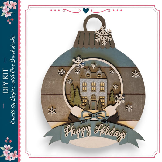 A decorative ornament with a snow globe containing a house and trees, surrounded by snowflakes. The ornament has a ribbon with the text "Happy Holidays" and a heart symbol.