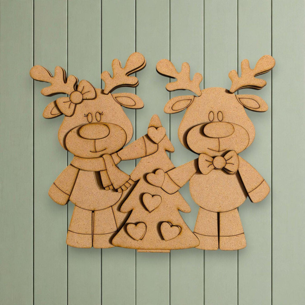 A wooden cutout of two cartoon reindeer standing next to a Christmas tree, with hearts on the tree.