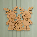 A wooden cutout of two cartoon reindeer standing next to a Christmas tree, with hearts on the tree.