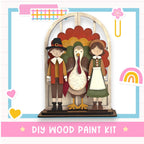 A DIY wood paint kit featuring a wooden frame with a turkey, a boy in a red and brown outfit, and a girl in a green dress, set against a colorful background.