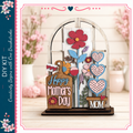 A wooden display with a floral design and the text "Happy Mother's Day" on it, placed on a wooden surface.