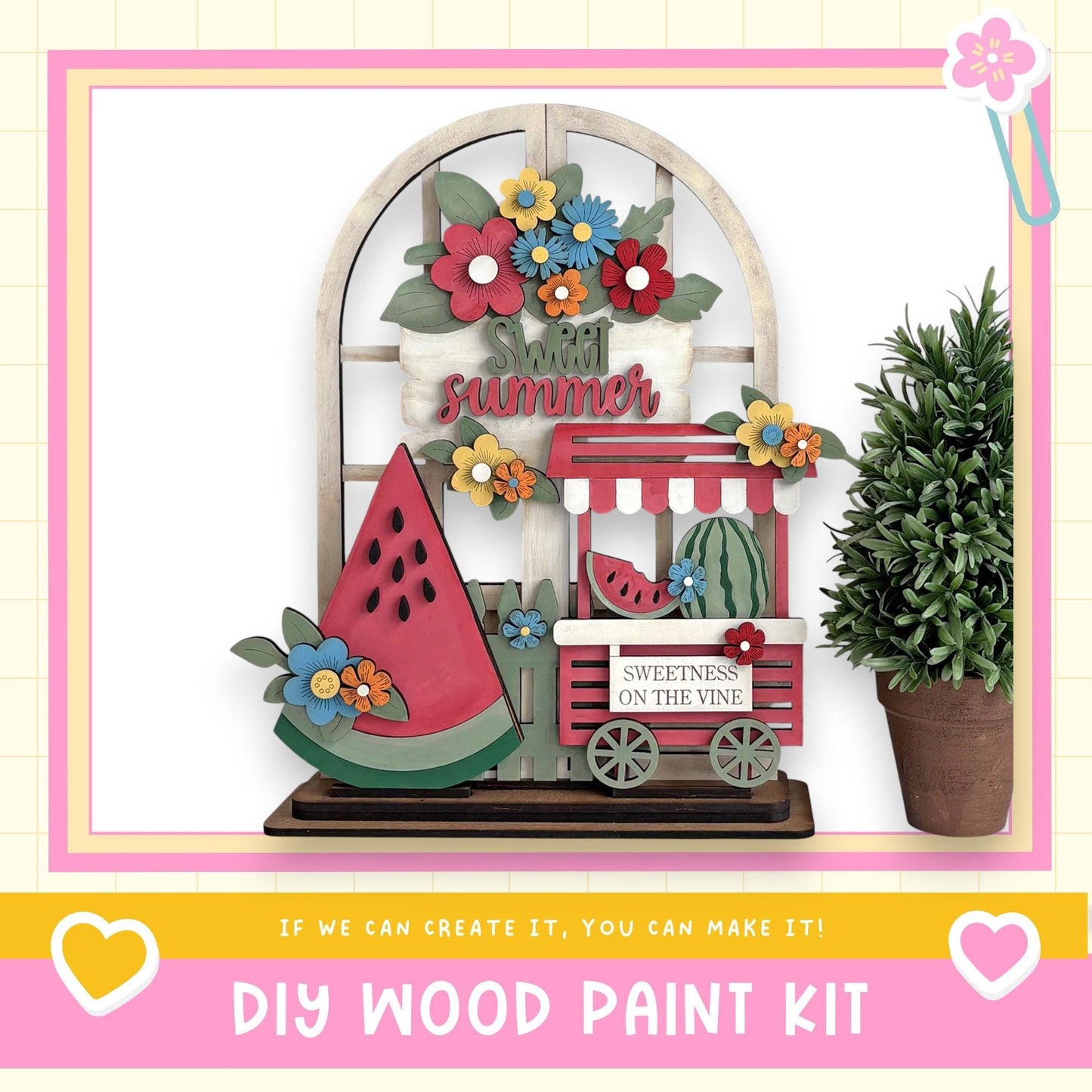 a DIY wood paint kit for creating a summer-themed decoration, including a wooden sign with the word "summer" and a wooden wagon with a watermelon on top. The kit is displayed in a pink frame, and there is a potted plant next to it.