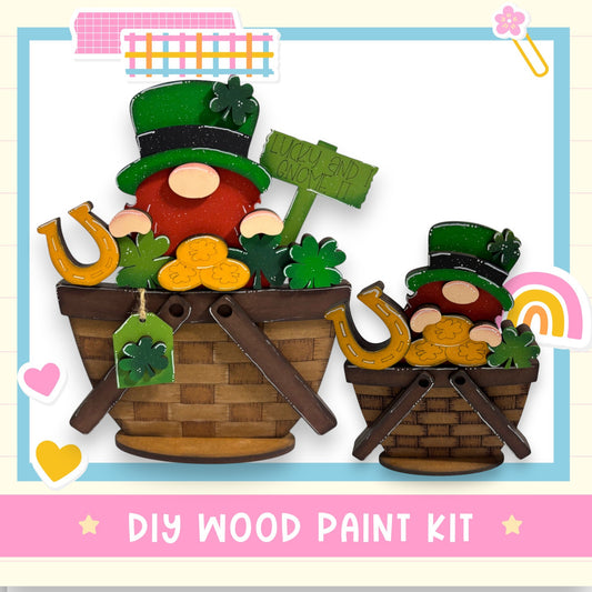 two wooden gnome figurines, each wearing a top hat and holding a sign that says "Lucky and Good". The gnomes are sitting in baskets filled with various objects, such as a horseshoe, a clover, and a rainbow. The image also includes a DIY wood paint kit and the text "DIY WOOD PAINT KIT".
