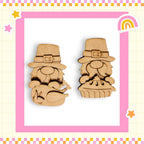two wooden gnome figurines wearing hats, one with a pie in its hands, set against a pink and yellow checkered background with stars and a rainbow.