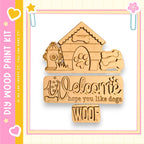 a wooden sign with the text "Welcome hope you like dogs" carved into it, along with a dog house and fire hydrant. The sign is surrounded by a pink and yellow border, and there are small decorative elements such as hearts and flowers on the border.