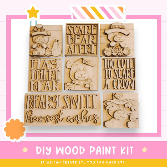 The image is a DIY wood paint kit featuring various wooden cutouts with text and illustrations, including a bear, a scarecrow, and a bird.