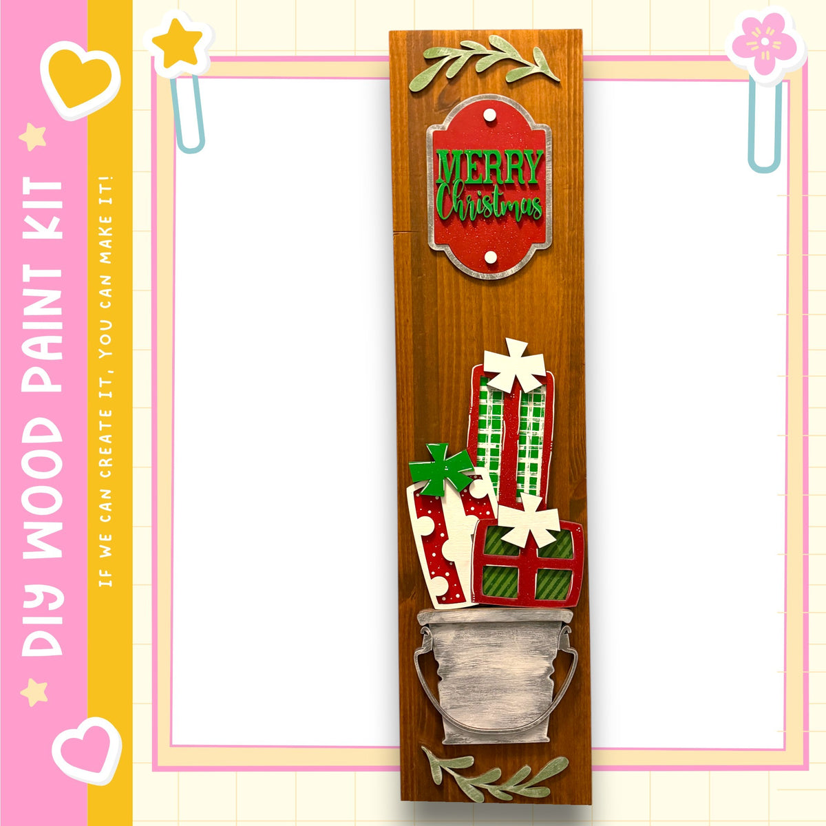 a wooden frame with a decorative design, including a vase with wrapped gifts and a "Merry Christmas" sign. The frame is set against a pink and yellow background with a heart and star motif.