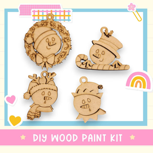 The image is a collage of four wooden ornaments, each featuring a different design, including a snowman, a reindeer, a Santa hat, and a rainbow. The text "DIY WOOD PAINT KIT" is displayed at the bottom of the image.