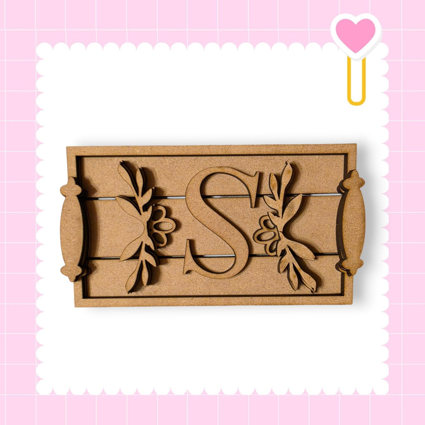 A wooden tray with a decorative letter 'S' on it, set against a pink background with a heart shape.