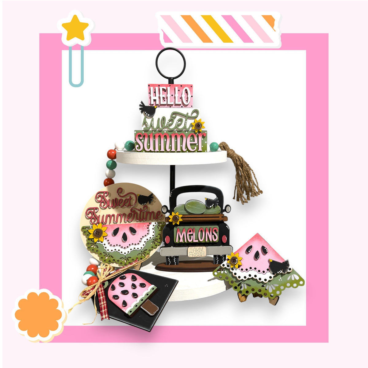 A colorful and whimsical arrangement of summer-themed objects, including a star, a sign, a wagon, and a watermelon, all set against a pink background.