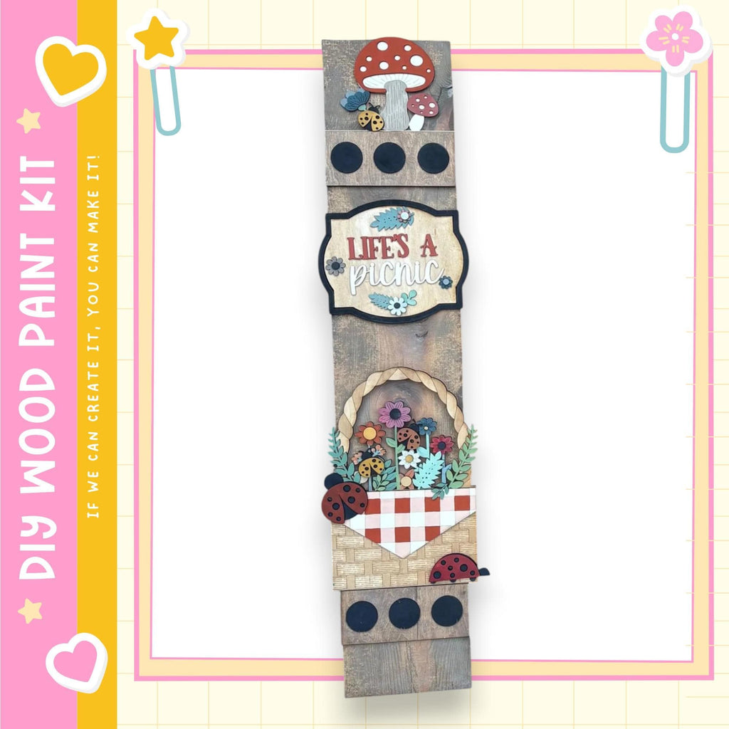 The image is a wooden sign with various decorative elements, including a mushroom, flowers, and ladybugs, mounted on a wooden frame.