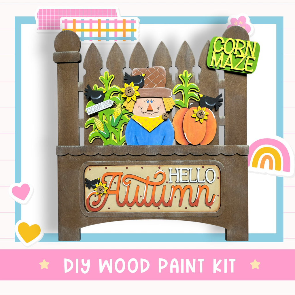 The image is a DIY wood paint kit for creating a fall-themed decoration, featuring a scarecrow, corn maze, and a sign that says "Hello Autumn".