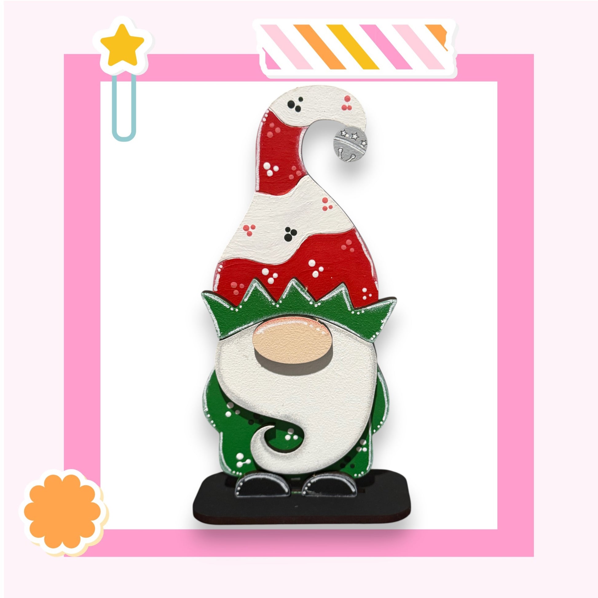 A colorful gnome figurine with a red and white hat and green beard stands against a pink background.