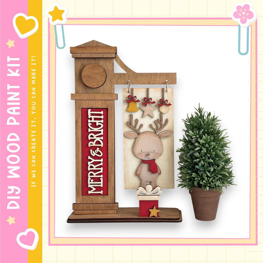 a wooden clock with a deer figure on it, placed next to a potted plant. The clock has a sign that says "MERRY & BRIGHT".