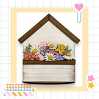 A wooden house-shaped planter filled with a variety of colorful flowers, including daisies, roses, and other blooms.
