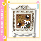 a decorative wooden frame with a floral design and the text "bee kind" written on it. The frame is set against a white background, and there are small flowers and bees on the frame.