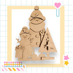 A cardboard snowman and a cardboard Christmas tree are depicted in the image, set against a grid background with various colorful stickers.