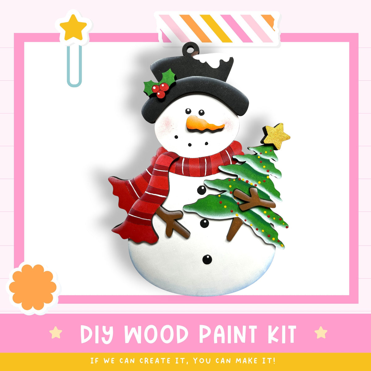 A colorful wooden snowman ornament with a Christmas tree, a star, and a black hat, set against a pink background.