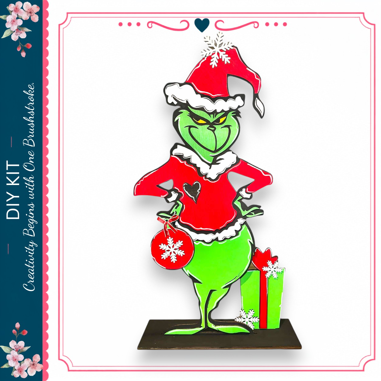A green Grinch figure wearing a red Santa hat and holding a red gift box with a snowflake design, standing on a black base.