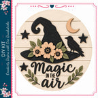 a wooden sign with a black witch's hat, flowers, and a bird, along with the text "Magic in the air".