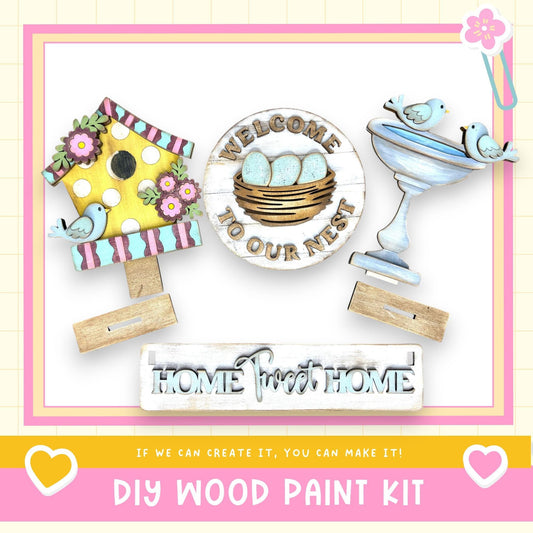 The image is a DIY wood paint kit featuring a birdhouse, a sign that says "Welcome to our nest", and a sign that says "Home sweet home". The kit appears to be made of wood and is designed to be used as a decoration or home improvement project.