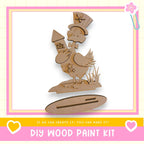 a DIY wood paint kit, with a wooden duck holding a rocket ship and a star on its back, set against a pink and yellow background.