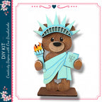 A teddy bear wearing a blue dress and holding a torch, representing the Statue of Liberty.
