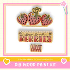 The image is a promotional poster for a DIY wood paint kit, featuring a wooden strawberry decoration and the text "Farm fresh berries sweet" along with a heart symbol.