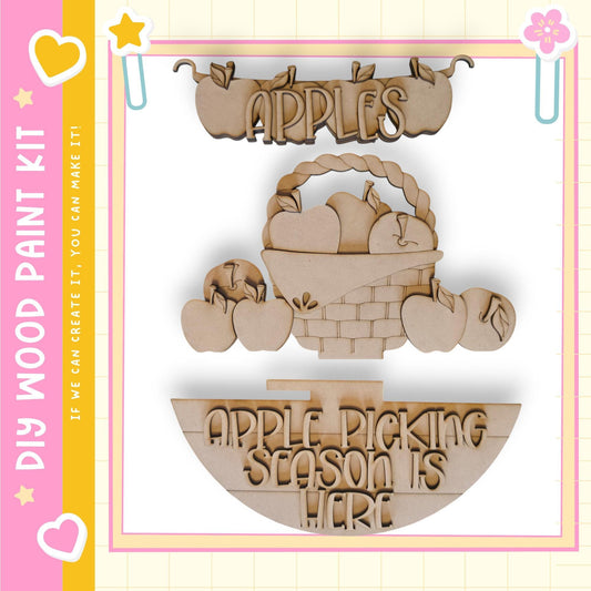 a wooden sign with the text "APPLES" and "APPLE PICKING SEASON IS HERE" carved into it. The sign is made of wood and appears to be a decorative piece.