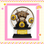 A wooden snow globe containing a cartoon cow with horns and a flower, surrounded by sunflowers.
