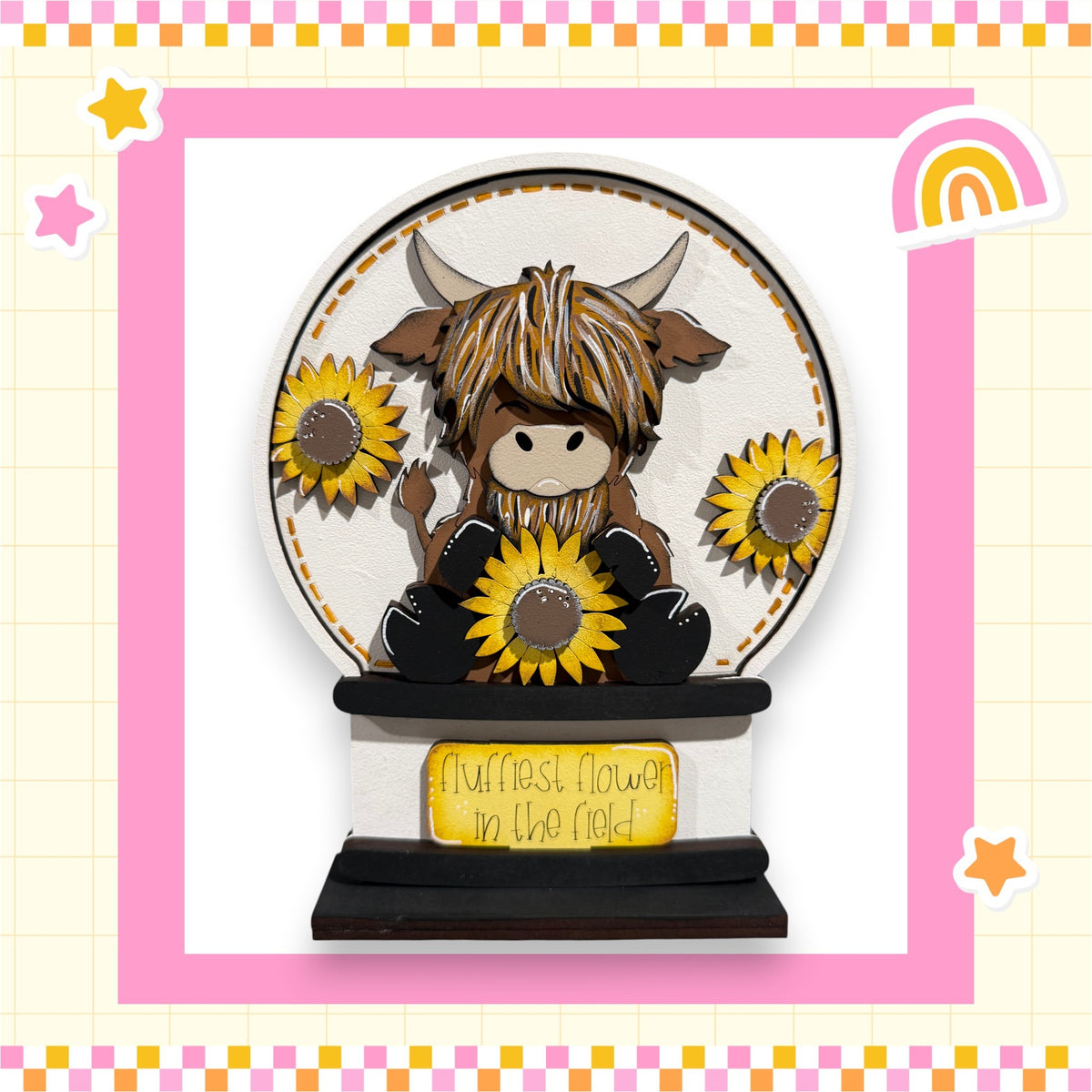 A wooden snow globe containing a cartoon cow with horns and a flower, surrounded by sunflowers.