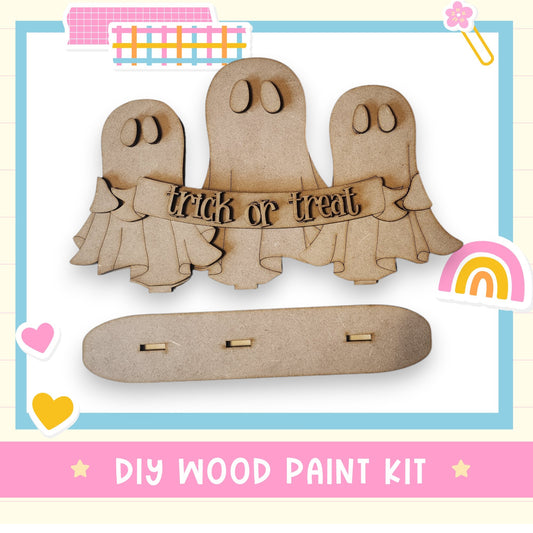 a wooden cutout of three ghost with a rainbow in the background