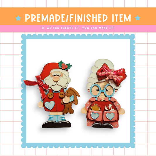 two wooden figurines, Santa Claus and an elderly woman, both wearing red outfits and holding small stuffed animals.