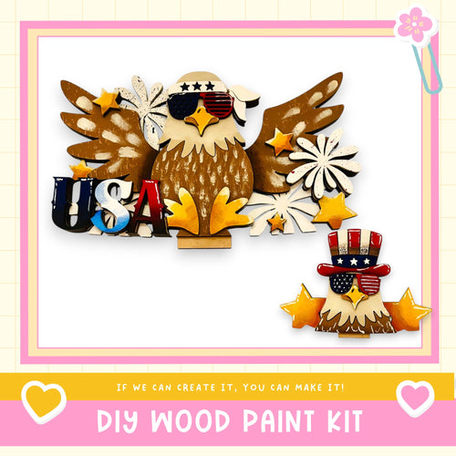 The image is a collage featuring a wooden eagle and a smaller wooden eagle, along with various patriotic symbols such as stars, flowers, and the word "USA". The collage is framed by a pink border and includes text that reads "DIY WOOD PAINT KIT" and "If we can create it, you can make it!".