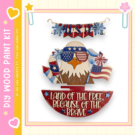 a patriotic design with a banner that says "USA" and a wooden eagle wearing sunglasses. The eagle is holding a flag and a sign that says "Land of the free because of the brave". The design is framed by a pink border with a yellow stripe.