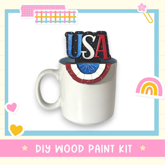 A white mug with the word "USA" painted on it, surrounded by various colorful stickers and a "DIY WOOD PAINT KIT" label.