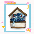 A wooden house-shaped object with the text "RED white & BOOM" written on it, surrounded by various colorful and decorative elements such as hearts, a rainbow, and a flower.